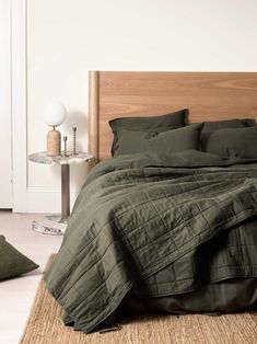 a bed with green linens and pillows in a white room next to a table