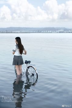 a woman standing in the water next to a bike