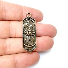 This celestial-themed pendant showcases an elegant design featuring the moon, sun, and stars, perfect for cosmic and boho-inspired jewelry pieces. The intricate detailing and antique copper-tone finish bring a vintage charm, making it ideal as a focal point for necklaces, keychains, or bracelets. Whether you're crafting for astrology lovers or creating mystical-themed accessories, this lightweight charm adds a magical touch to any creation. Material : Zamac, Nickel free and Lead free metal Color: Antique Copper Size : 44x14mm Celestial Moon And Sun, Moon Sun And Stars, Moon And Sun, Pendant Earring, Moon Sun, Earring Charms, Sun And Stars, Charm Making, Jewelry Making Charms