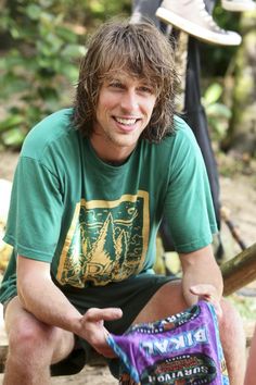 a man sitting on the ground holding a bag of chips