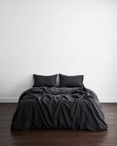 a bed with black sheets and pillows in a white room next to a wooden floor