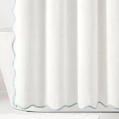 a white bath tub sitting next to a shower curtain with scalloped trim on it