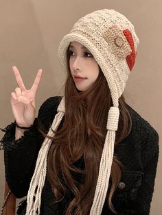 a woman with long hair wearing a knit hat and holding up the peace sign in front of her face