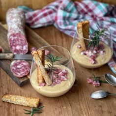 two glasses filled with food sitting on top of a wooden table next to utensils