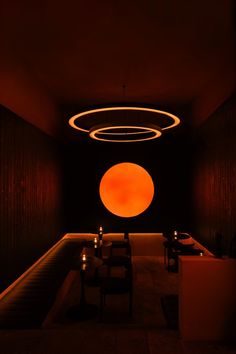 a dimly lit room with chairs and tables in front of an orange circle on the wall