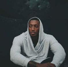 a man wearing a hoodie sitting on the floor in front of a black background