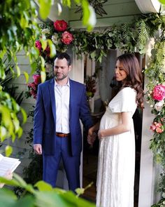 a pregnant woman standing next to a man in front of a doorway with flowers on it