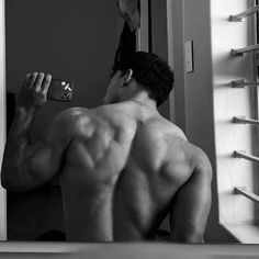 a shirtless man drinking from a bottle in front of a mirror with his back turned to the camera