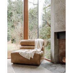 a chair with a blanket on it sitting in front of a fire place next to a window