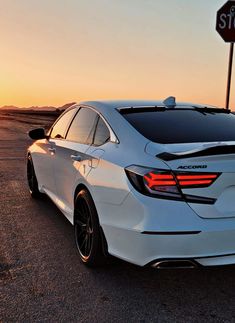 the rear end of a white car parked in front of a stop sign at sunset