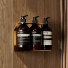 three bottles of aessop on a wooden wall next to a metal container with soap and lotion in it