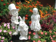 two statues of children with hats and tails are in the garden surrounded by colorful flowers