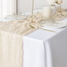 the table is set with white plates and flowers on it, along with gold place settings