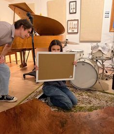 two people are sitting on the floor and one is holding up a large sheet of paper