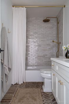 a bathroom with white and gold fixtures, tile flooring, shower curtain, toilet and bathtub