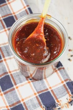 a wooden spoon in a jar filled with barbecue sauce on a checkered cloth tablecloth