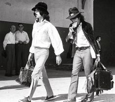 black and white photograph of two people walking down the street with luggage in their hands