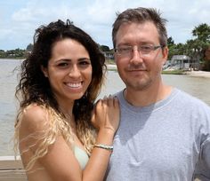 a man and woman standing next to each other on a pier near the water with palm trees in the background