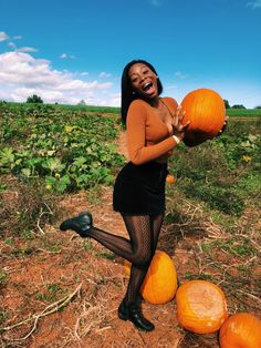 a woman is holding two pumpkins in her hands and posing for the camera on a field