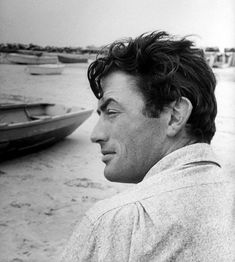 a black and white photo of a man on the beach with boats in the background