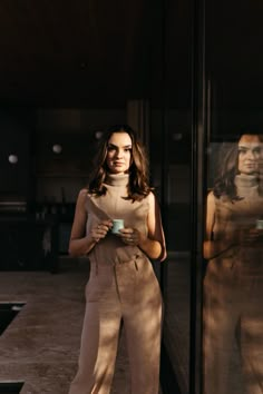 a woman standing in front of a window holding a cup