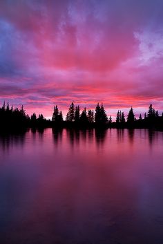 the sky is pink and purple as the sun sets in the distance over a lake