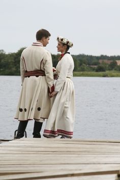 two people standing on a dock next to the water looking at each other and smiling