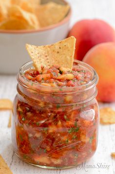 a glass jar filled with salsa and chips on top of a table next to an apple