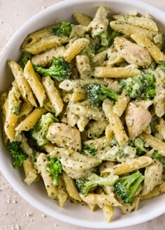 a white bowl filled with pasta and broccoli on top of a marble counter