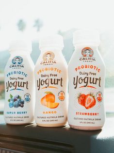 three bottles of yogurt sitting on top of a window sill