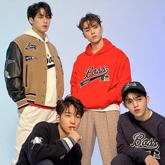 four young men are posing for a photo in front of a blue background, one is wearing a red hoodie and the other wears a brown jacket