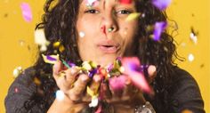 a woman is blowing confetti on her face and looking surprised at the camera