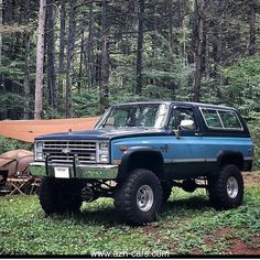 a blue truck parked in the woods next to a camper with a tarp on top