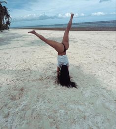 a woman doing a handstand on the beach with palm trees in the background