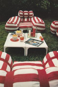 red and white striped couches sitting on top of a grass covered field next to a table