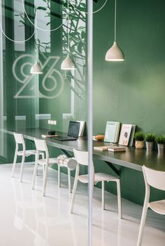 an office with green walls and white chairs in front of a table that has two laptops on it