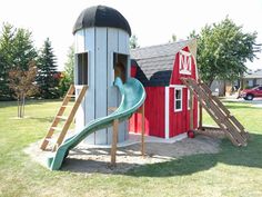 a play structure with a slide in the grass next to a red barn and green roof