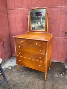 an old dresser with a mirror on it next to a chair and a red wall