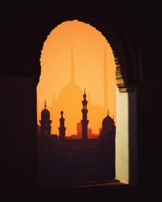 the sun is setting behind an arch in a building with domes and minarets