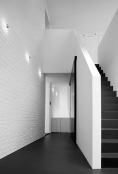 an empty room with white brick walls and black flooring, along with stairs leading up to the second floor