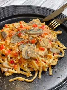 a black plate topped with pasta covered in mushrooms and tomato sauce next to a fork