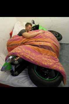 a man laying on top of a motorcycle covered in a blanket