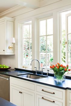 a kitchen with white cabinets and black counter tops, along with a bowl of fruit on the sink