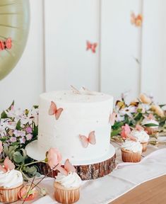 a white cake sitting on top of a table next to cupcakes and flowers