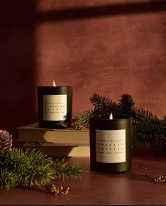 two candles sitting on top of a wooden table next to pine cones and evergreen branches