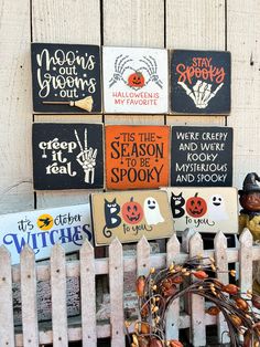 halloween signs are on display in front of a white picket fence with a wreath next to it