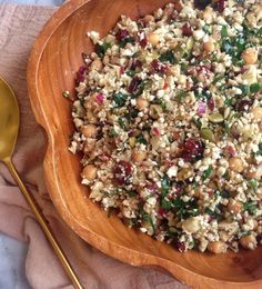 a wooden bowl filled with food on top of a pink towel next to a gold spoon