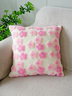 a pink and white pillow sitting on top of a couch next to a potted plant