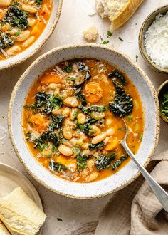 two bowls filled with shrimp and spinach soup on top of a white table next to bread