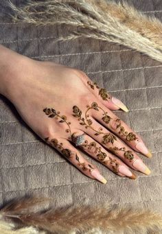 a woman's hand with hennap and flowers painted on it, next to some feathers